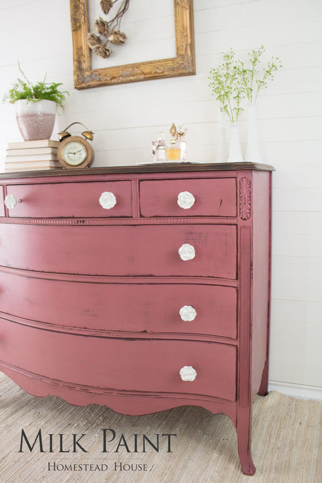 Vintage pink dresser in Homestead House Texas Rose Milk Paint with white knobs, books, and plants on top.