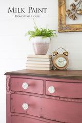 Mauve dresser in Texas Rose Milk Paint by Homestead House with white knobs, books, clock, and fern.