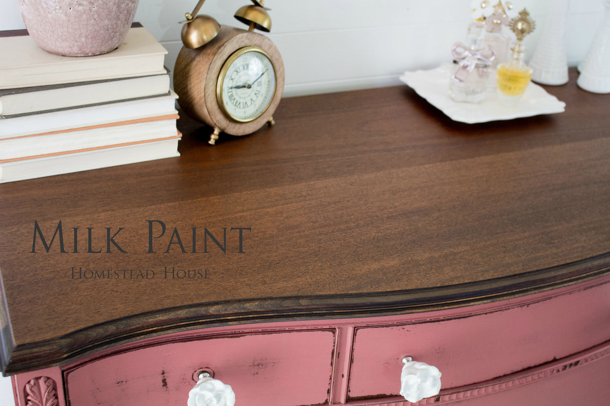 Wood dresser with dark top, drawers in Homestead House Texas Rose Milk Paint, white knobs, books and decor on top.