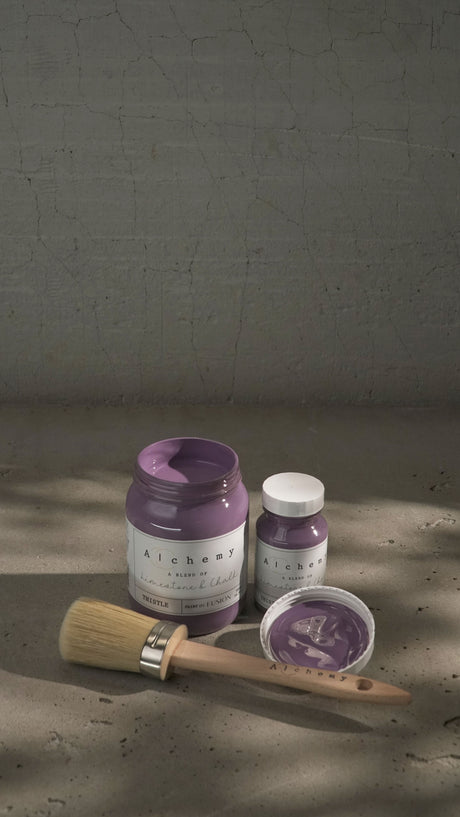 Three jars of Thistle Alchemy Paint by Fusion Mineral Paint, one open, with a paintbrush nearby.