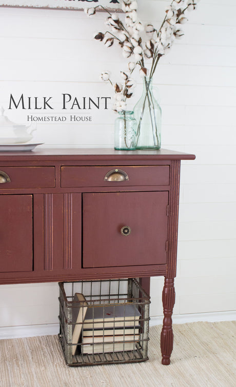Homestead House Trading Post Red Milk Paint sideboard with brass handles, topped with glass cotton stems and books.
