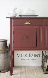 Homestead House Trading Post Red Milk Paint sideboard beside a milk can, topped with white dishes.