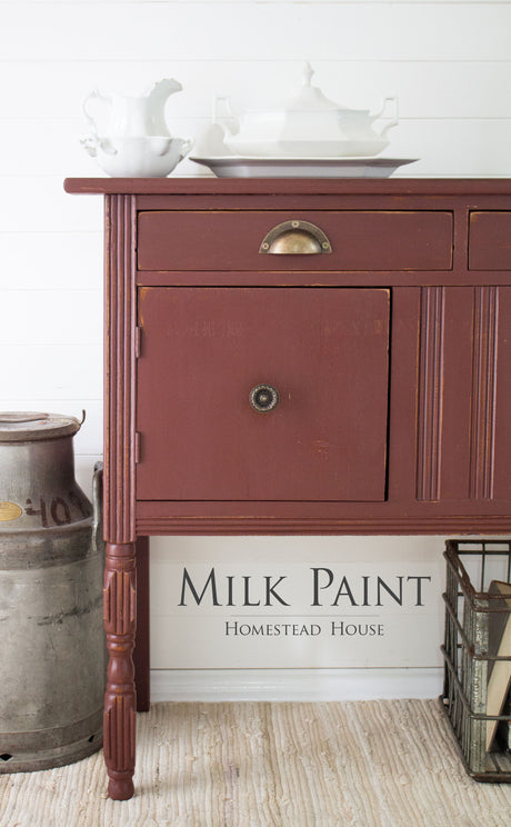 Homestead House Trading Post Red Milk Paint sideboard beside a milk can, topped with white dishes.