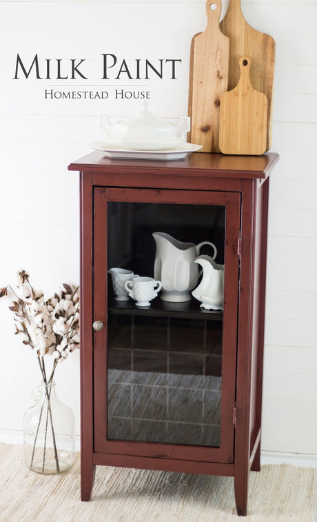 Small cabinet in Homestead House Trading Post Red Milk Paint, with white dishes and cutting boards on top.
