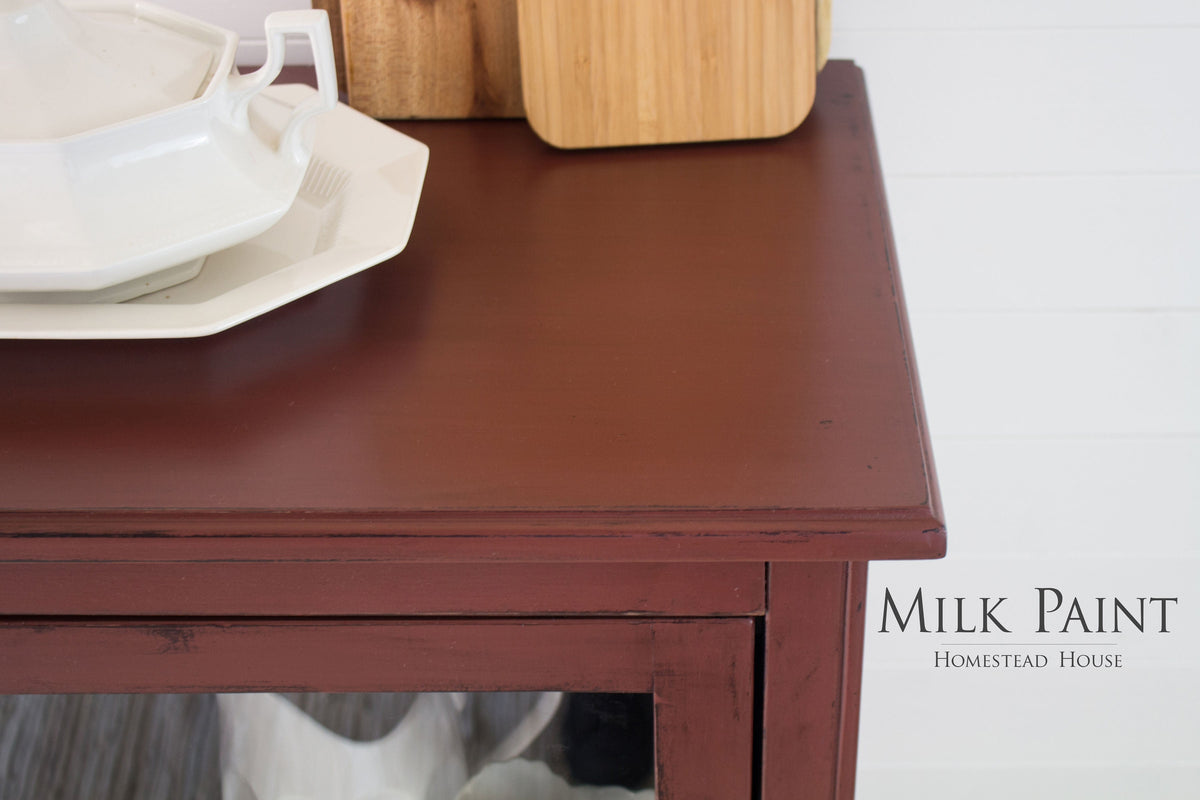Trading Post Red Milk Paint wooden cabinet by Homestead House, with white dishes; brand text at lower right.