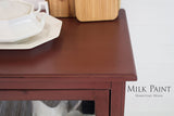 Trading Post Red Milk Paint wooden cabinet by Homestead House, with white dishes; brand text at lower right.
