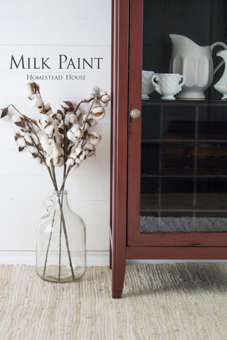Clear glass jug with cotton stems next to a cabinet painted in Homestead House Trading Post Red Milk Paint.