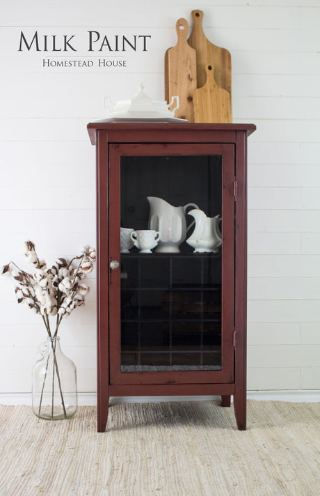 Cabinet painted Trading Post Red Milk Paint by Homestead House, with dishes inside; boards and vase nearby.
