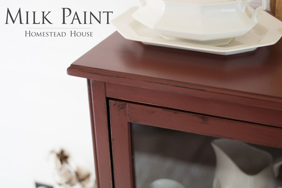 Maroon cabinet in Trading Post Red Milk Paint by Homestead House, topped with white dishes.
