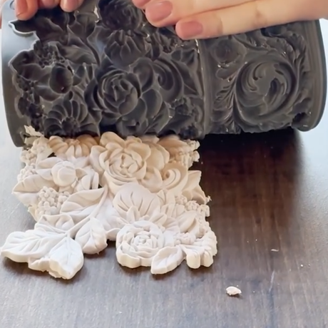 Hand presses Trimmings 4 Mould by IOD onto clay on wood, creating a raised floral and leaf design.