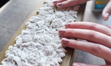 Hands smoothing a white relief design made with I.O.D. Trimmings 4 Mould on a rectangular surface.