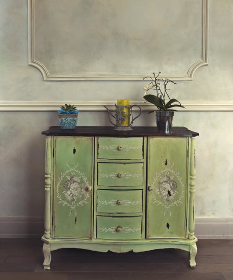 Green vintage cabinet with IOD Laurel Paint Inlay, topped with three plants and a yellow candle.
