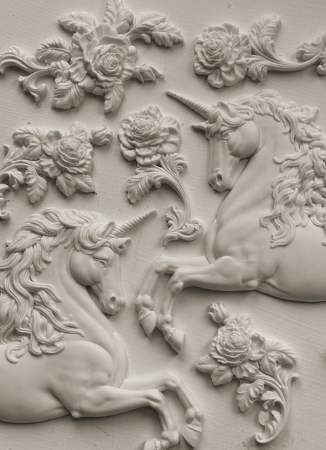 Two white-relief unicorns and flowers made with the Unicorns Mould by IOD on a flat surface.