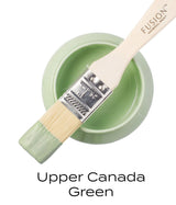 Fusion Mineral Paint jar in Upper Canada Green (Seasonal) with a brush resting on top, bristles dipped in paint.