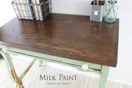 Wooden desk with dark top, legs in Homestead House Upper Canada Green milk paint, white knobs, books, and jars.