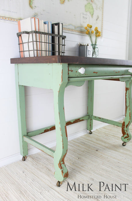Distressed desk in Upper Canada Green Milk Paint with books, a map, and vase on top.