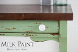 Green distressed wooden table with a dark brown top, finished in Homestead House Upper Canada Green Milk Paint.