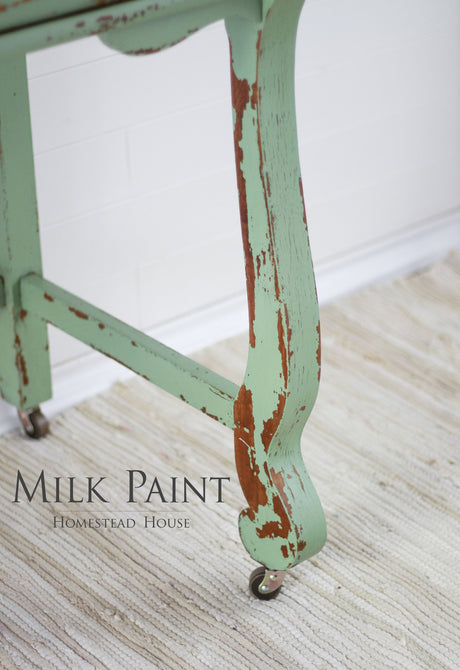 Table leg on wheels with chipped Upper Canada Green Milk Paint by Homestead House, on beige rug.
