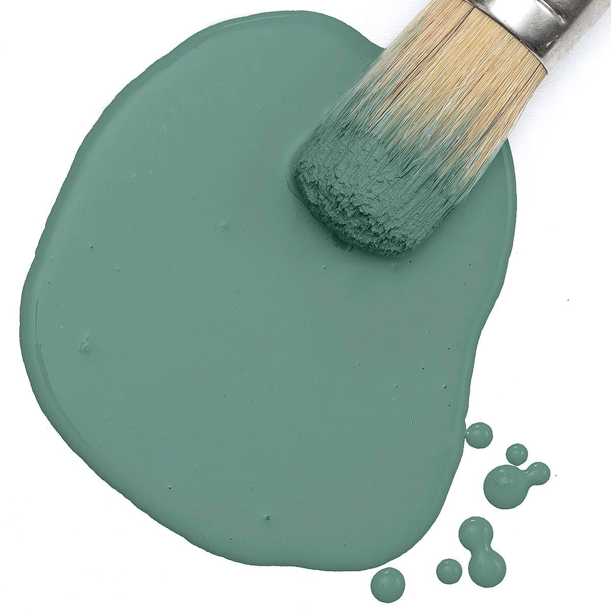 Paintbrush dipped in Velvet Palm Paint by Fusion Mineral Paint, with teal splatters on a white background.