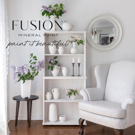 White armchair and shelf painted in Victorian Lace by Fusion Mineral Paint, logo near a round mirror and lilacs.