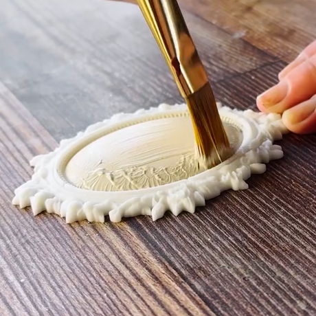 Hand painting an ornate oval frame from the I.O.D. Vintage Brooches Mould by Iron Orchid Designs on dark wood.