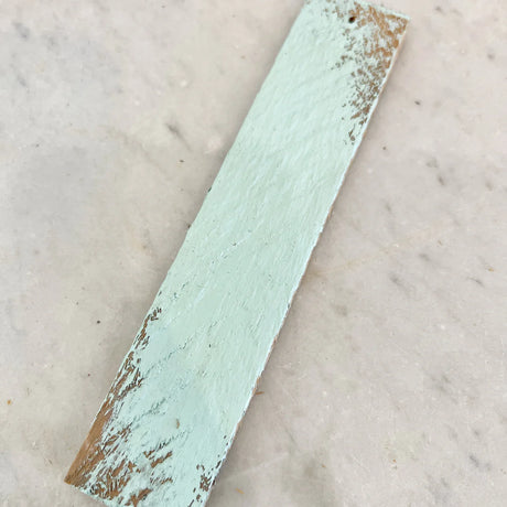 Narrow wood piece with chipped Vintage Mint DIY Cottage Color by DIY Paint Co. on light textured surface.