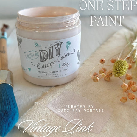 Open jar of Vintage Pink DIY Cottage Color by DIY Paint Co. with brush, dried flowers, and cloth nearby.