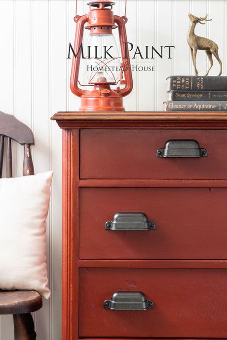 Red dresser in Homestead House Voyageur Milk Paint with black pulls; lantern, books, and deer figurines nearby.