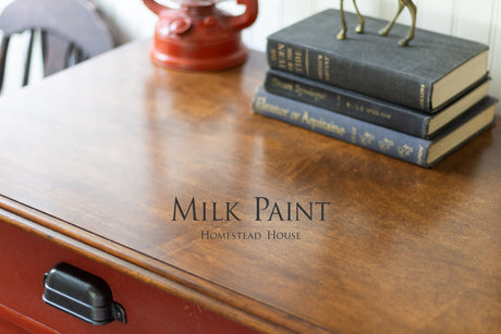 Wooden desk with books, red lamp, and “Voyageur Milk Paint by Homestead House” printed on the tabletop.