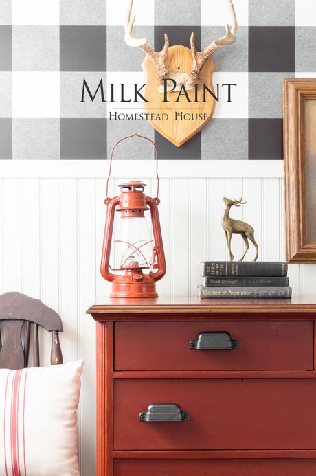 Red dresser painted with Homestead House Voyageur Milk Paint, set against a plaid wall with antlers above.