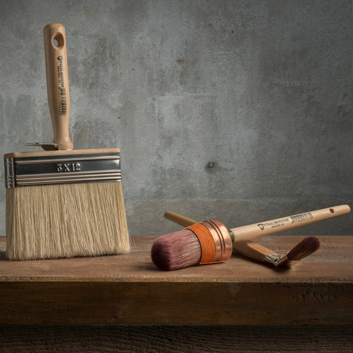Three brushes, including a Staalmeester Wall Brush Series 3005, displayed on wood.