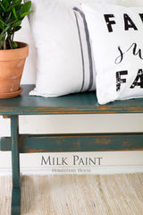 Bench painted in Waterloo Green Milk Paint by Homestead House with plant, pillows, and text reading Homestead House.