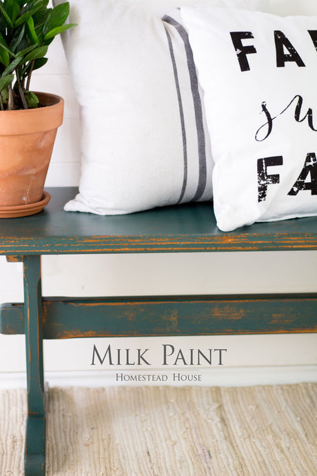 Bench painted in Waterloo Green Milk Paint by Homestead House with plant, pillows, and text reading Homestead House.