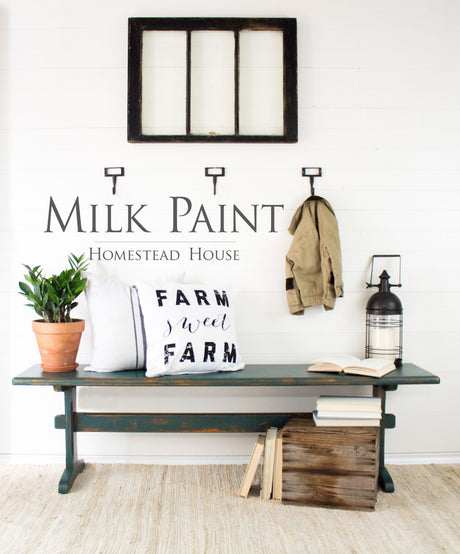 Bench with pillows, books, and plant under hooks; walls painted Homestead House Waterloo Green Milk Paint.