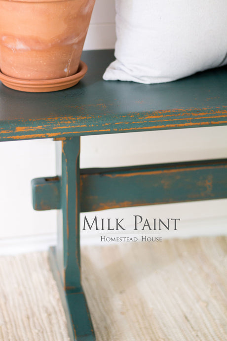 Distressed bench in Waterloo Green Milk Paint by Homestead House, with terracotta pot and white cushion.
