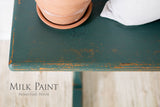 Green table in Waterloo Green Milk Paint by Homestead House, with terracotta pot and gray cushion; brand name visible.