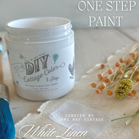 DIY Paint Co. White Linen Cottage Color paint jar with brush, fabric swatch, and dried flowers nearby.