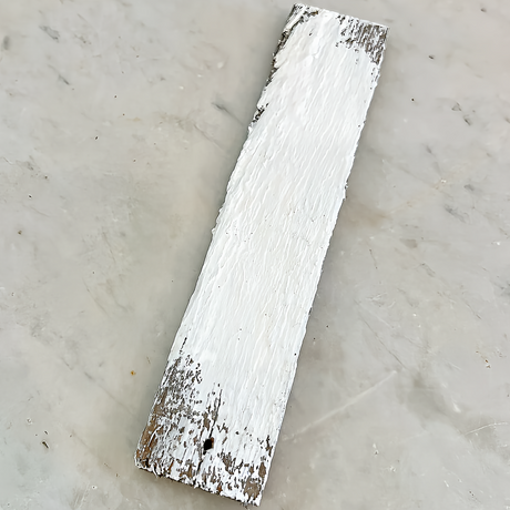 Rectangular wood piece with peeling White Linen DIY Cottage Color by DIY Paint Co. on a gray surface.