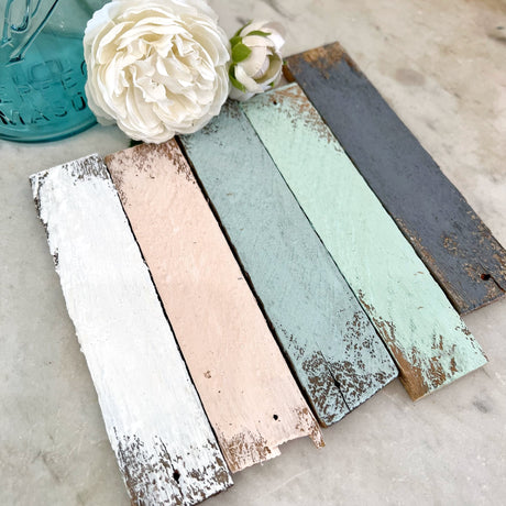 Five planks painted with White Linen DIY Cottage Color by DIY Paint Co., shown beside white flowers.