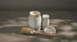 Three White Oak Alchemy Paint jars by Fusion Mineral Paint on gray surface, one jar open with a brush.
