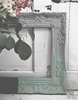 Ornate frame leaning on door finished with White Oil Wax by Old Fashioned Milk Paint, flowers placed nearby.