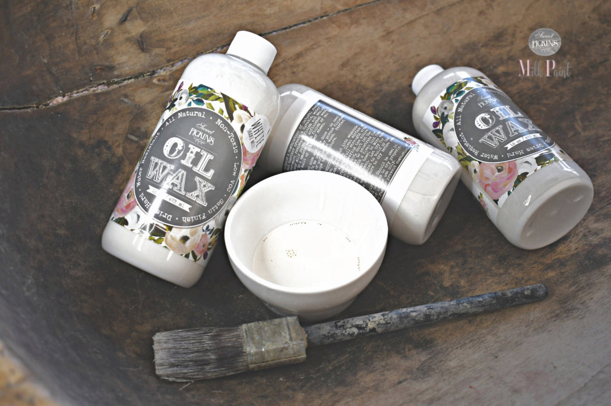 Three Sweet Pickins White Oil Wax bottles with a white bowl and brush on a wooden surface.