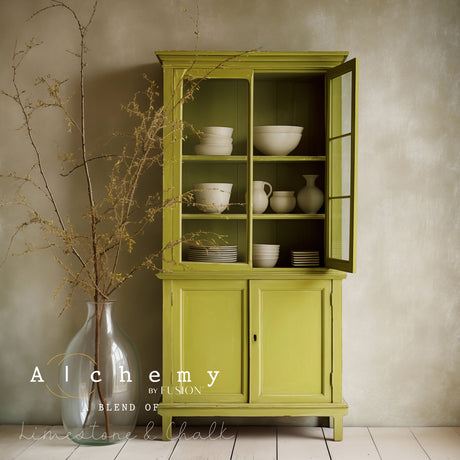 Green wooden cabinet in Willow Alchemy Paint by Fusion Mineral Paint holding white dishes, vase with branches beside it.