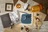 Willowbank Fusion Mineral Paint jar on a wooden table with brushes, books, whiskey, and sheet music nearby.