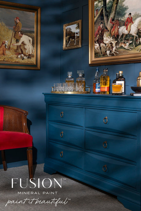 Willowbank Fusion Mineral Paint dresser with drinks, next to a red chair and dark blue paneled wall.