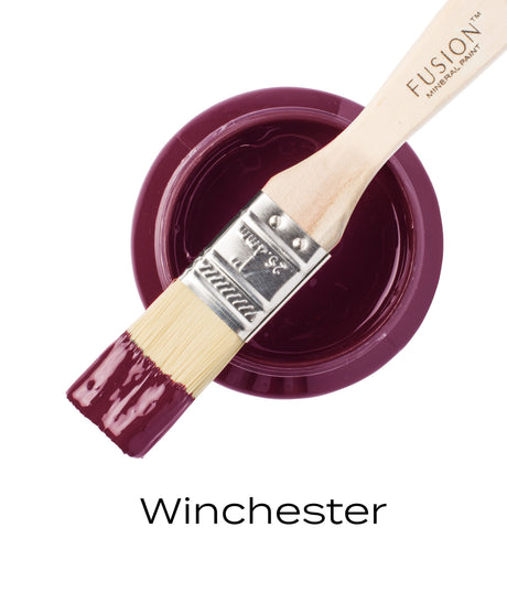 Paintbrush with plum-colored paint on open Winchester Fusion Mineral Paint jar; “Winchester” text below.