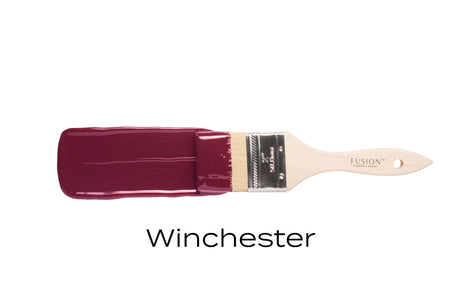 Paintbrush with dark red Winchester Fusion Mineral Paint by Fusion Mineral Paint on a white background.