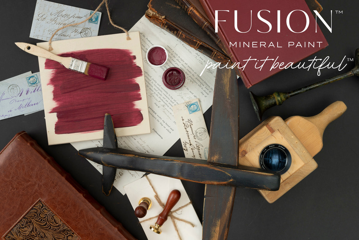 Open jars of Winchester Fusion Mineral Paint with brushes, old books, and wax seals arranged on a dark table.