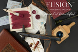 Open jars of Winchester Fusion Mineral Paint with brushes, old books, and wax seals arranged on a dark table.