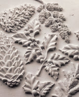 Pinecones and holly leaves crafted using I.O.D. Winter Forage Mould (2025 Limited Release) on white textured surface.